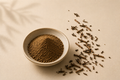 Existence Brewed Stillpoint roasted hōjicha green tea powder in a bowl with scattered roasted tea leaves.